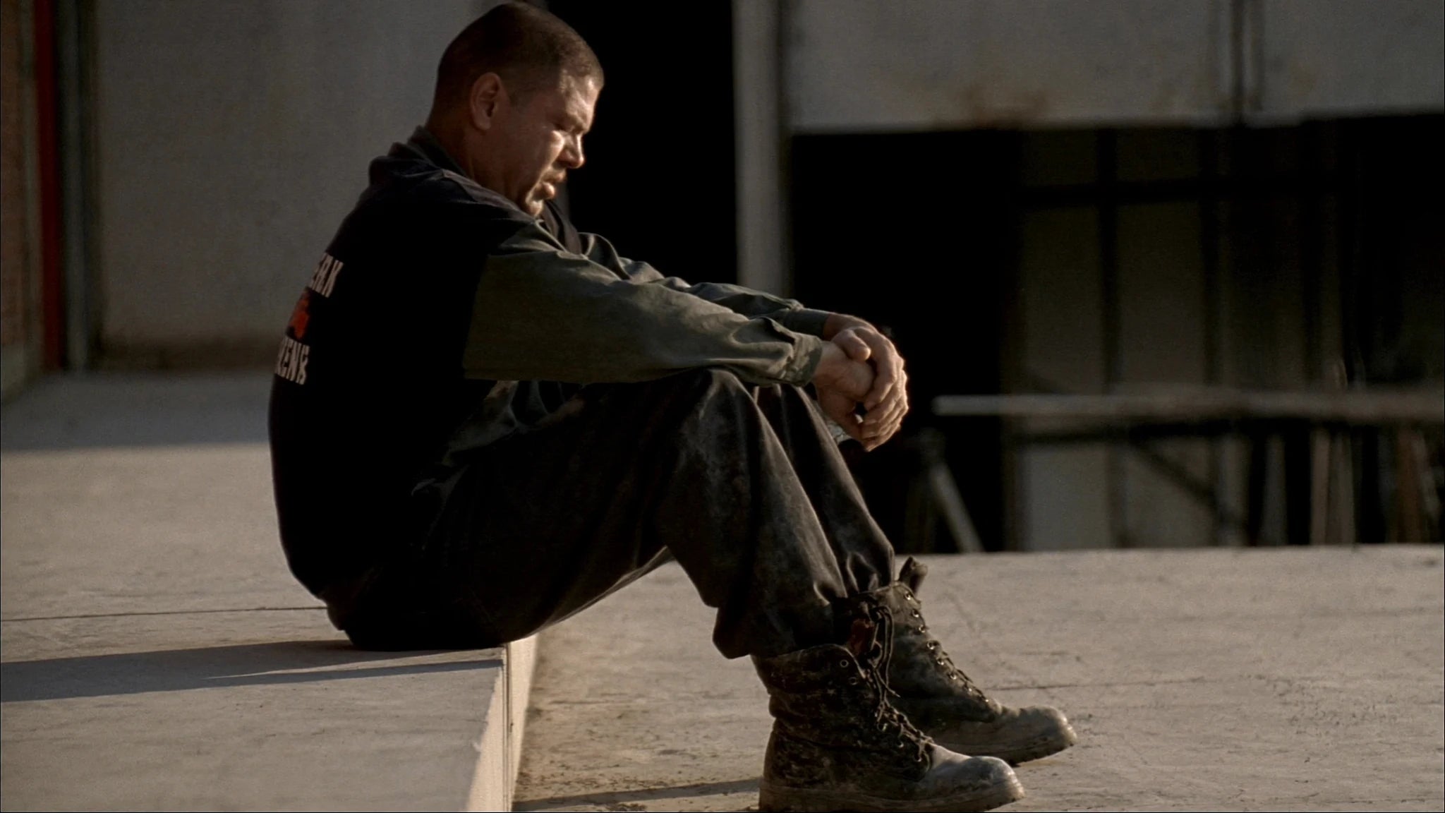 Tradesperson at end of a long shift, sitting on concrete, worn work boots, quiet exhaustion